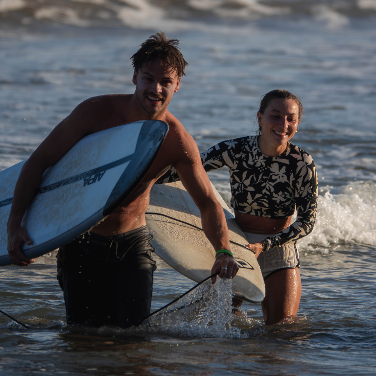 Two guests walking out of the ocean with surfboards after a lesson at Elsewhere Surf Camps